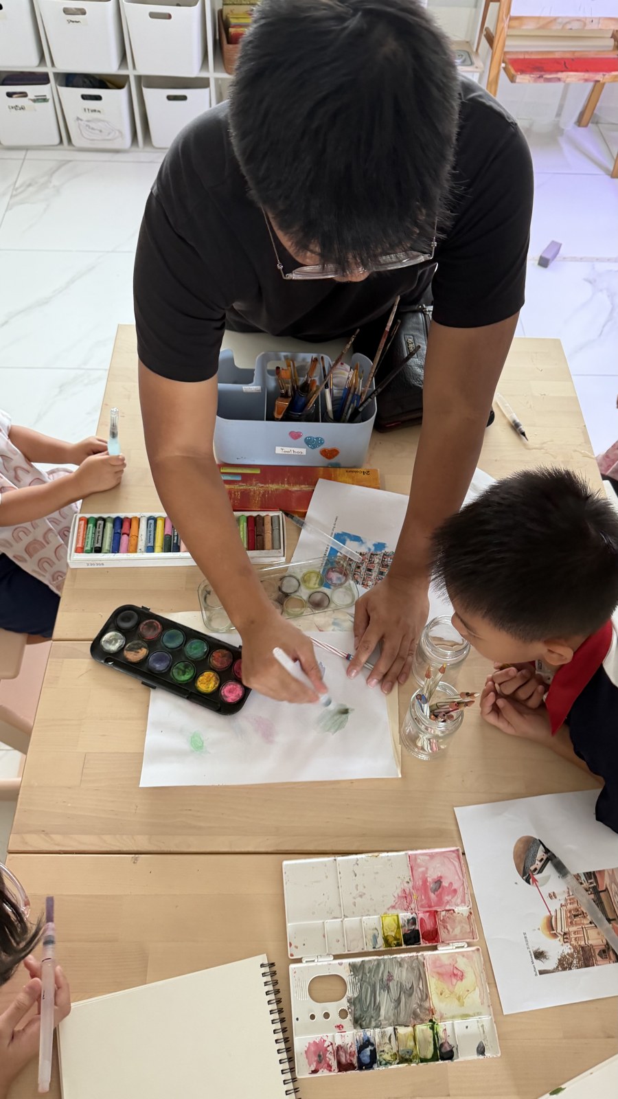 An adult and children painting with watercolours at a table