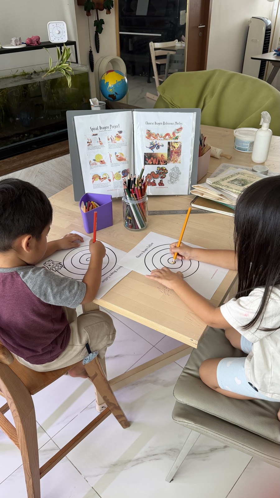 Two children drawing and painting at a table with books and art materials