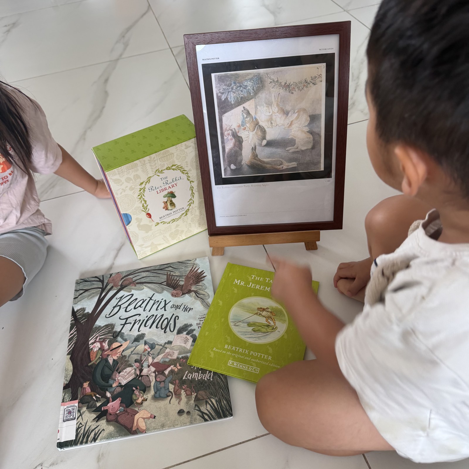 Children looking at Beatrix Potter books beside a framed illustration