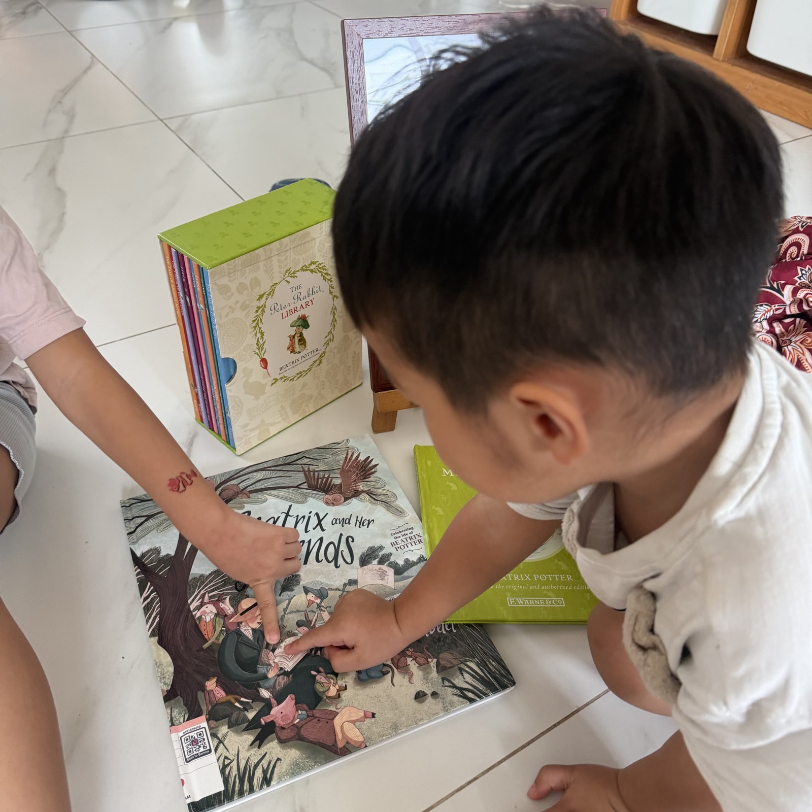 A child browsing Beatrix Potter books on the floor