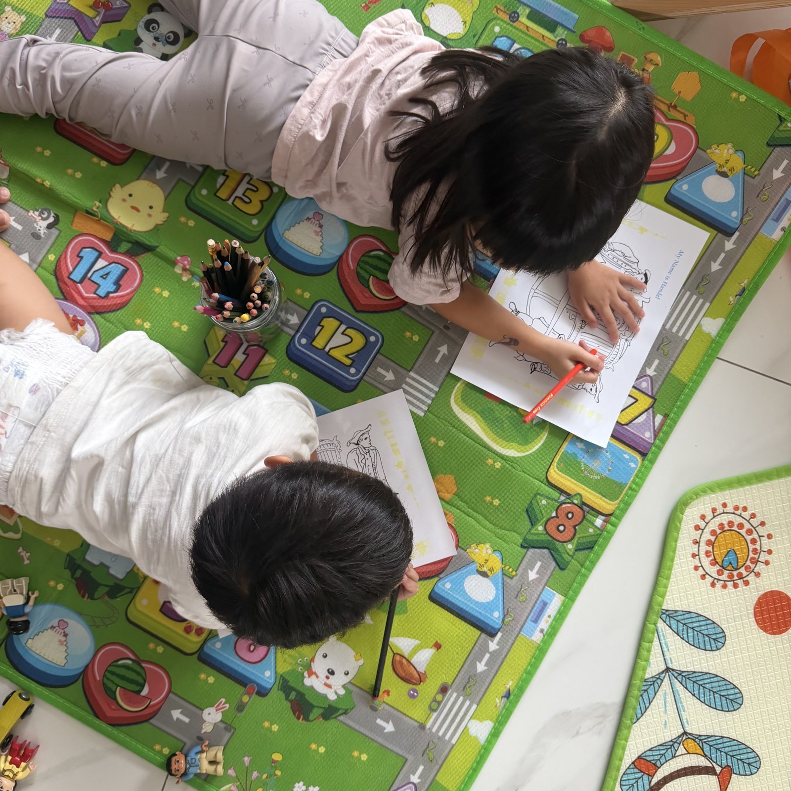 Children lying on a play mat with a notebook and coloured pencils